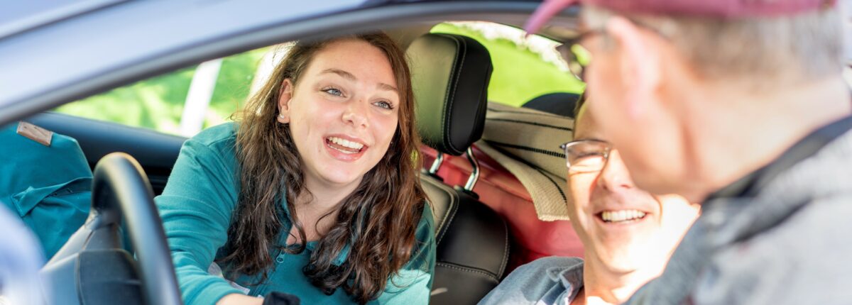 President Pribbenow is reaching into a parked car past the driver to shake hands with a student.